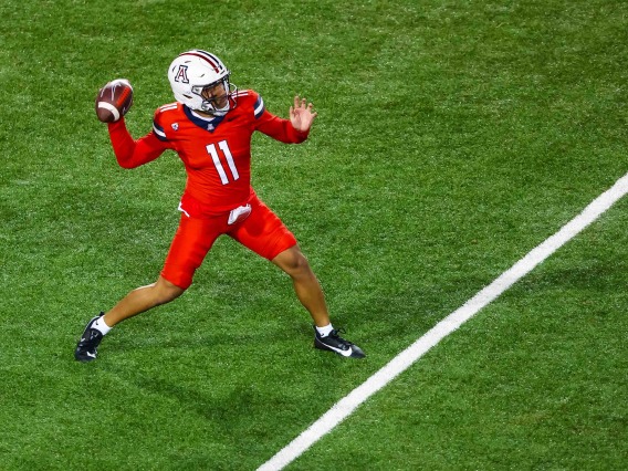 A football player in red throws a ball on a green field