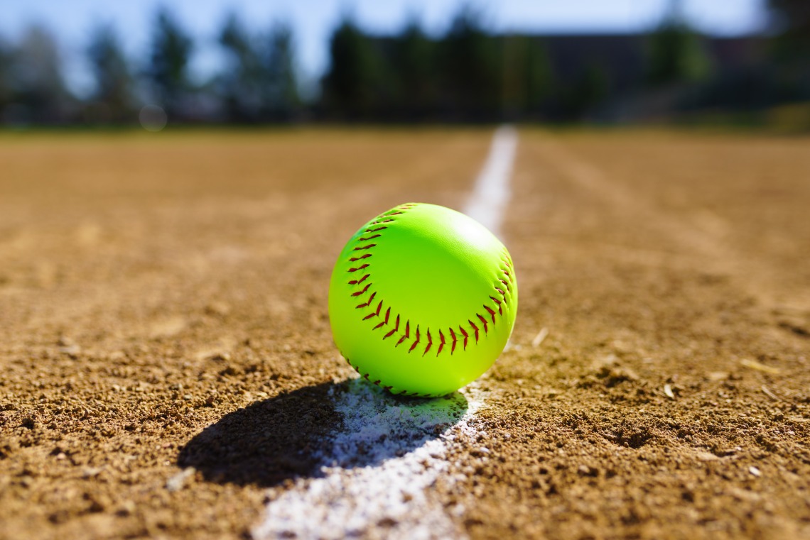 A photograph of a bright yellow softball on a field 