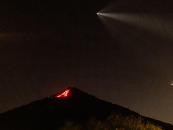 The "A" on Sentinel Peak lit up with flares as a SpaceX rocket flies above