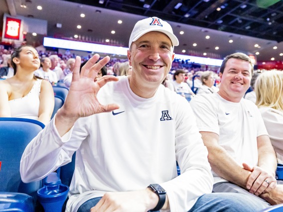 A photograph of a man wearing a white UArizona shirt and white UArizona hat holding up a Wildcat sign