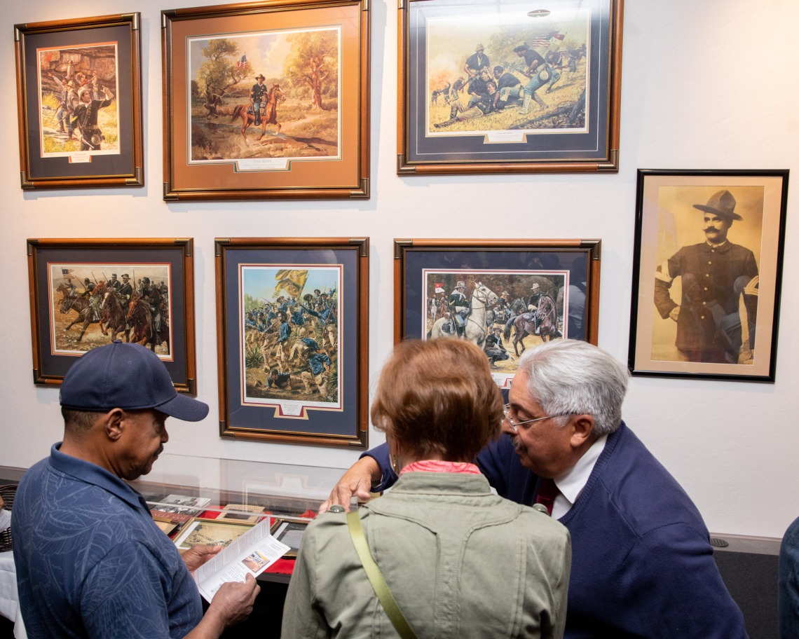 A photograph of an exhibit filled with photos and paintings with guests learning at the African American Museum of Southern Arizona.