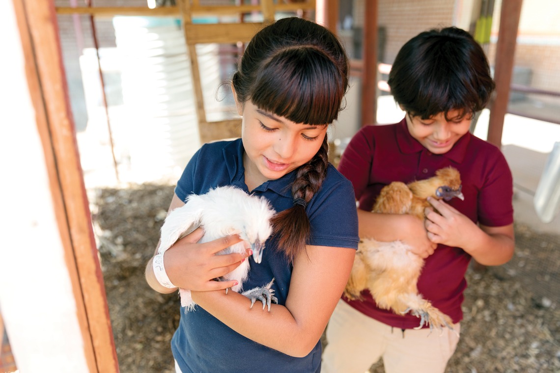 A photograph of two Manzo Elementary students hugging and admiring chickens