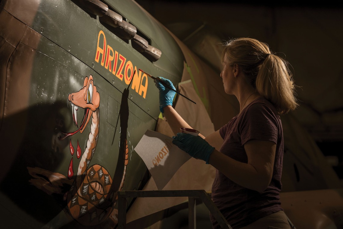 A photograph of a woman painting 'Arizona' on an aircraft