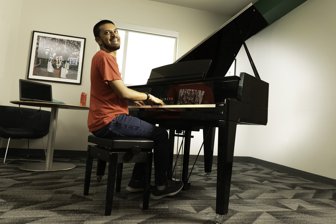 A photograph of a student sitting, smiling and playing the piano 