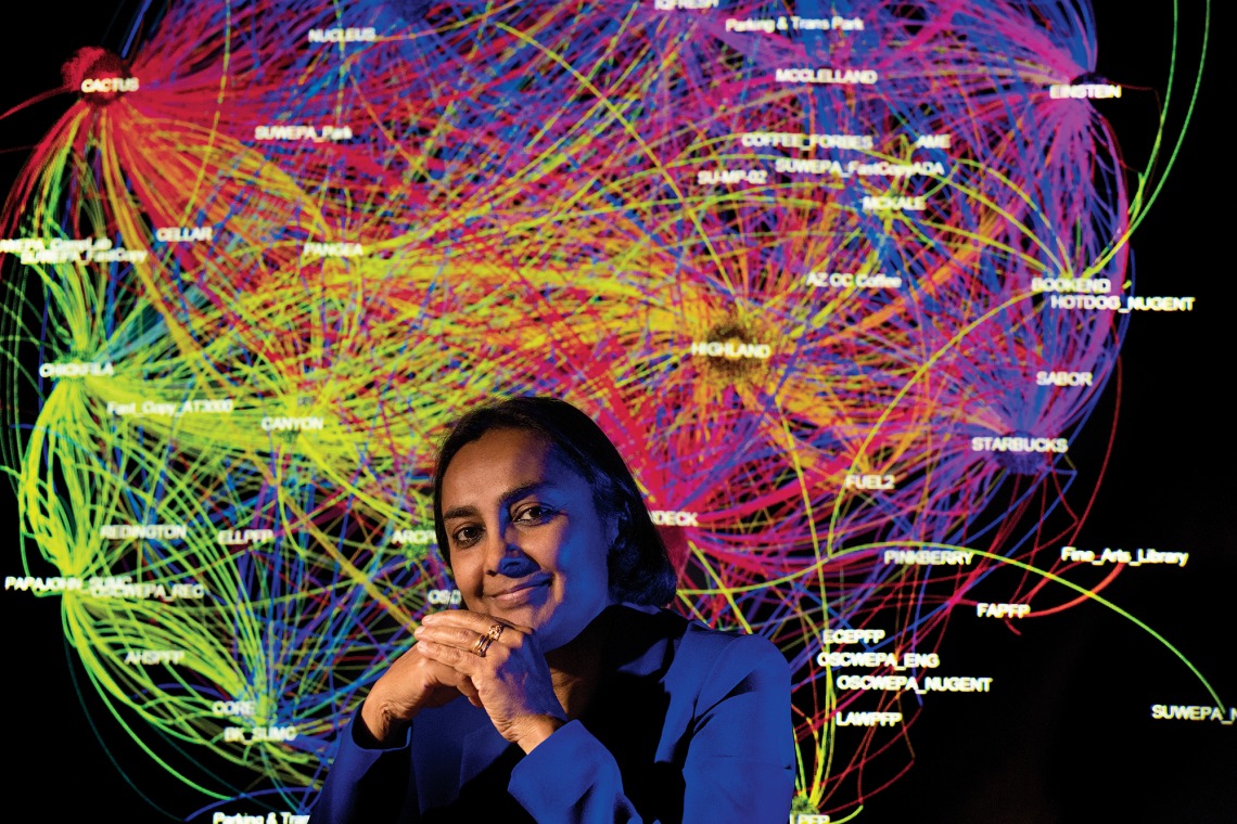 A photograph of Sudha Ram, sitting in front of a colorful backdrop illustrating data