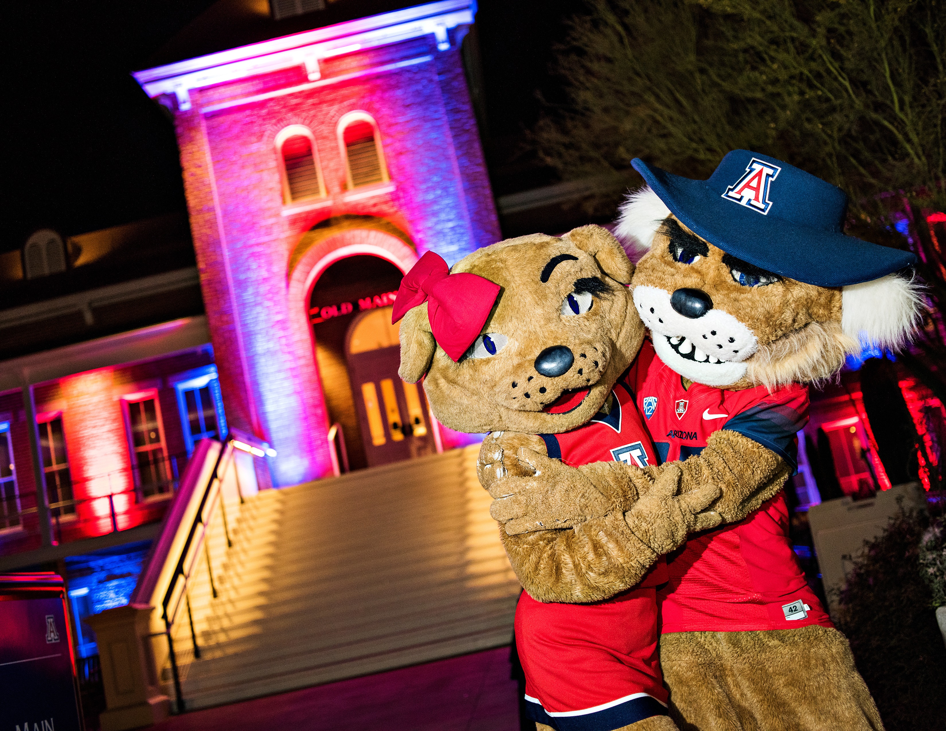 Wilbur and Wilma Wildcat mascots hugging in front of Old Main