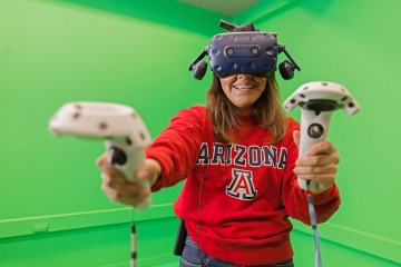 A photograph of a student, who is smiling, using the Virtual Reality headset and controllers 