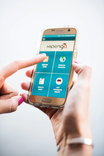 A photograph of a hand holding a phone on the app's homepage